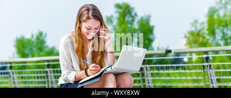 panoramic view on dynamic young executive girl taking notes on her agenda, outside. Symbolizing a job search or a trade of outsourcing Stock Photo