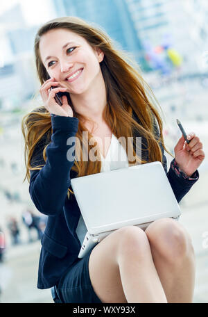 dynamic young executive girl on the phone consulting her laptop. Symbolizing a job search or a trade of outsourcing Stock Photo