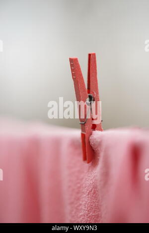 Red clothespin holds pink clothes on a rope, macro photo. Stock Photo