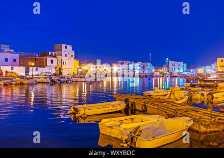 BIZERTE, TUNISIA - SEPTEMBER 4, 2015: Watch the evening city from the port with many moored fishing boats and bright city lights, reflected on water s Stock Photo