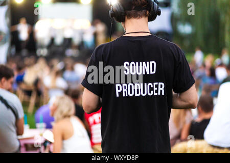 Technician guy in headphones and t-shirt with the inscription sound producer on his back at a outdoor show. Stock Photo