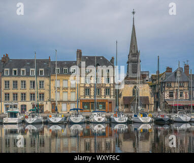 Sailboats line the quay below historic buildings and the Church of Saint Etienne reflected in the still water of the Old Harbor in Honfleur, France Stock Photo