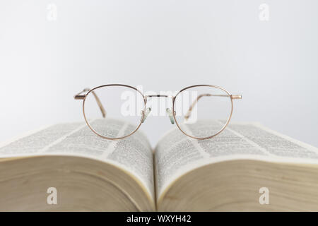 Close-up of a woman reading glasses in an open book on a white background Stock Photo