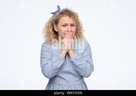 Shocked curly blonde girl covers her mouth with hands, isolated on white Stock Photo