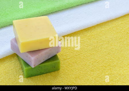 Stack of green, purple and yellow handmade soap bars on a yellow, white and green terry towels. Natural toiletries and hygiene products with herbs. Stock Photo