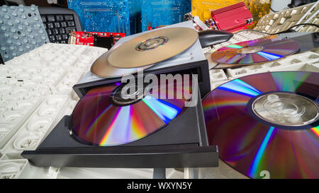 Compact discs and keyboards in a heap of old computer parts. E-waste sorting and recycling. Obsolete digital data storage device in CD drive. Ecology. Stock Photo