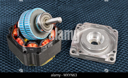 Disassembled electric step motor parts on a dark grid background. Blue rotor with steel shaft on black stator with inductors and copper wire windings. Stock Photo