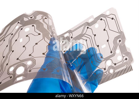 Plastic flex printed circuit board. Human hand in blue glove. Engineer holding a bent membrane of dismantled computer keyboard. Brown copper PCB layer. Stock Photo