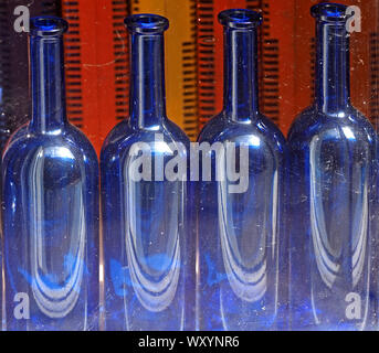 light reflecting on curves of four uncorked blue glass bottles with orange and red background creates bold pattern in Fife,Scotland, UK Stock Photo