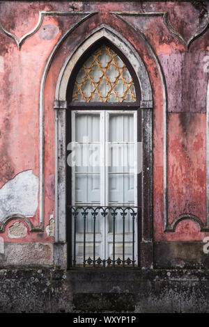 Elegant, tall, old arched window with metal balcony and peeling painted pink / red walls on residential property in Rua da Trindade, Sintra, Portugal Stock Photo