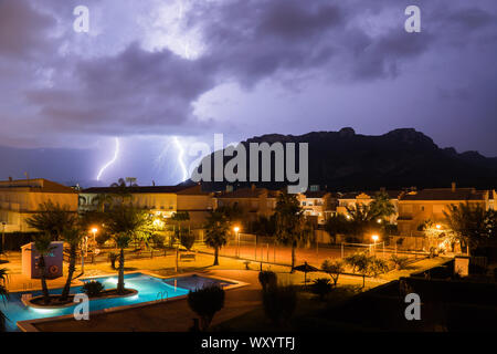 El Verger,Spain-August 27,2019-a lightning strikes from stromy clouds over a village with a pool and mountains Stock Photo