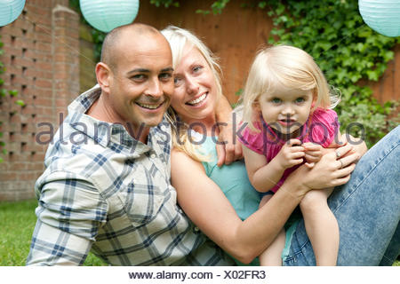 Portrait of happy couple sitting with toddler daughter in garden