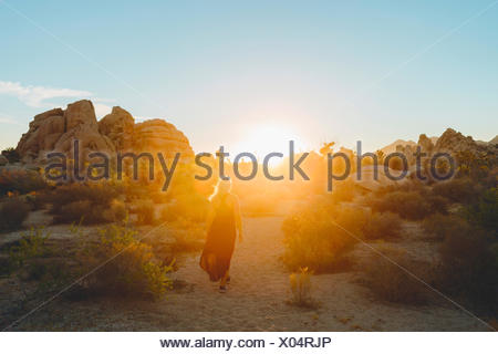 USA, California, Joshua Tree National Park, Woman wearing dress hiking at sunset