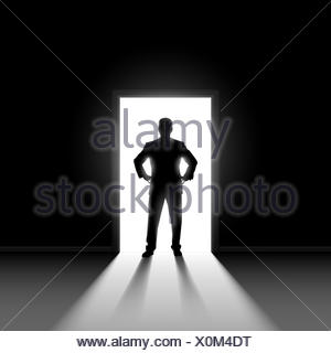 Silhouette of business man entering dark room with bright light in ...