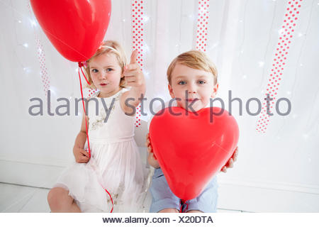 Young boy and girl posing for a picture in a photographers studio, holding red balloons.