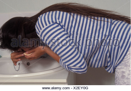 pregnant woman suffering from nose bleed bending over sink Stock Photo