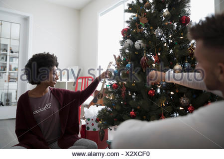 Young Couple In Pajamas Decorating Hanging Ornaments On