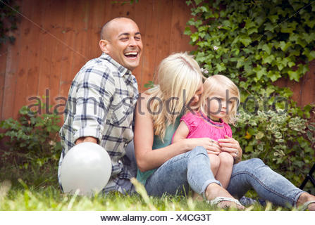 Happy couple sitting with toddler daughter in garden
