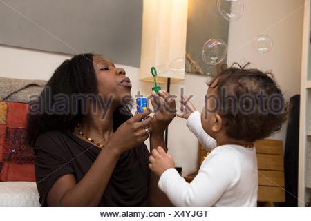 Mid adult woman and toddler daughter blowing bubbles