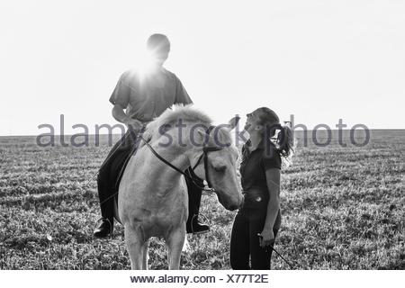 B&W image of woman chatting with man riding grey horse in field