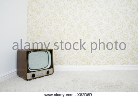Retro television in corner of room with patterned wallpaper