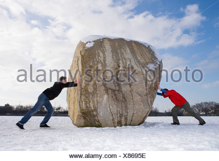 Young man pushing a large snow ball. Evergreen forest in the Stock ...