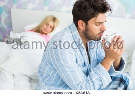 https://l450v.alamy.com/450v/x8a61a/sick-man-drinking-coffee-on-bed-while-woman-sleeping-in-background-at-home-x8a61a.jpg