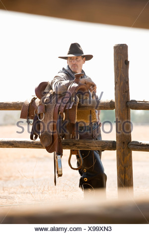 A rancher leaning against a saddle on a fence