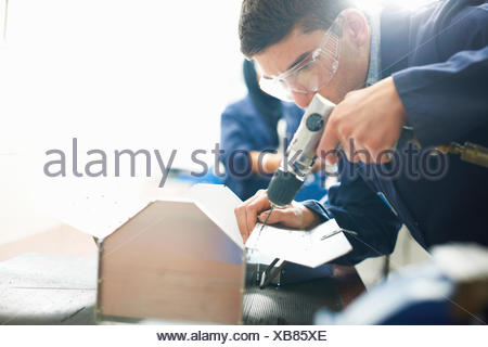 Male student using hand drill in college workshop
