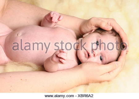 Ein kleines neugeborenes Baby liegt auf einem Schaffell. Sie Haende seiner Mutter umfassen zaertlich seinen Kopf.