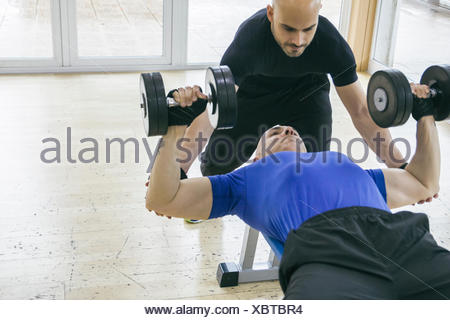 Man Lifting Weights Assisted By A Coach Lying On A Bench Gym Stock