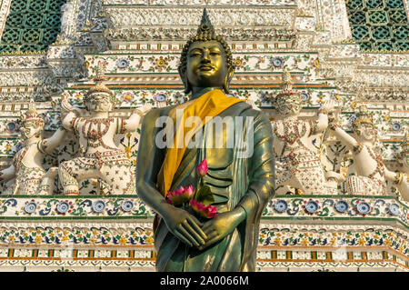 Stehender Buddha Skulptur im goldenen Gewand, kasaya gewickelt, mit Lotus Blumen in seine Hände gelegt. Wat Arun, Tempel der Morgenröte, Bangkok, Thailand Stockfoto