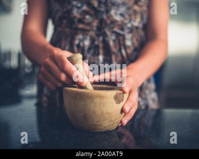 Eine junge Frau wird mit einem Stößel und Mörser in Ihrer Küche Stockfoto