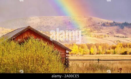 Einen schönen Herbst Landschaft Szene in ländlichen Wyoming, wie ein Regenbogen füllt den Himmel hinter einer alten Holzhütte. Stockfoto