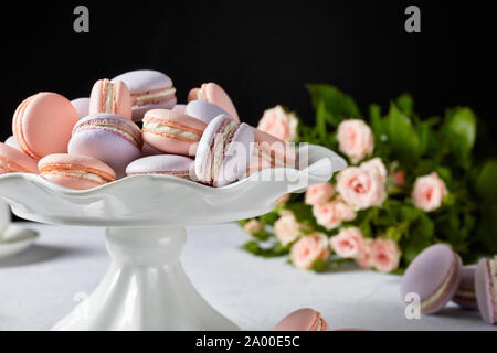 Macarons auf einem weißen stehen. Schönen Blumenstrauß aus Rosen auf dem schwarzen Hintergrund, horizontale Ansicht, close-up Stockfoto