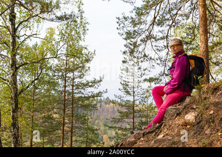 Frau Reisende sitzen auf einem Stein auf den Berg zu den Herbst Wald Stockfoto