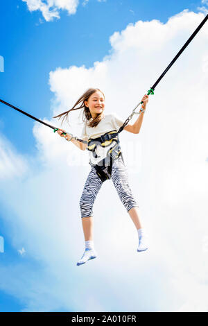 Kleines Mädchen springt hoch in die Luft mit einem Bungee Trampolin. Stockfoto