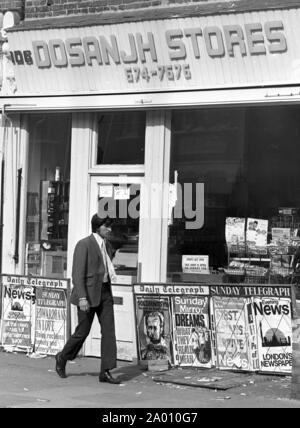Southall, London 1972. Eine elegant gekleidete junge Inder vorbei Dosanjh Geschäften und Zeitungsläden mit Zeitung Werbung einen, "Erste Asiaten anreisen..". Nach Idi Amin bestellt 30.000 Asiaten aus Uganda mit 90 Tagen, die mit britischen Pässen zu England geleitet. Sie wurden gezwungen, ihr Geld, Eigentum und Besitz hinter sich zu lassen. Diese Bilder dokumentieren das Leben für einige der Menschen, wie sie in Southall, westlich von London nieder. Einen Einblick in das Leben vor 47 Jahren für Einwanderer in Großbritannien. Foto von Tony Henshaw Stockfoto