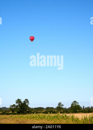 Eine rote Heißluftballon über Ackerland in der Nähe von Grantham in Lincolnshire gegen die lebendigen Clear blue sky Stockfoto