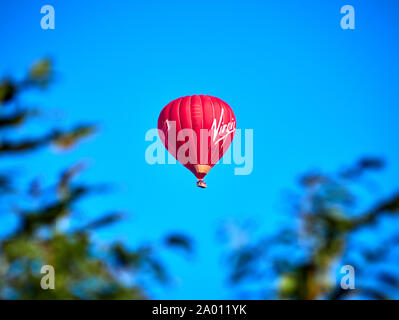 Eine helle rote Jungfrau heissluftballon gegen eine lebendige blauer Himmel von De gerahmte-fokussierten Niederlassungen Stockfoto