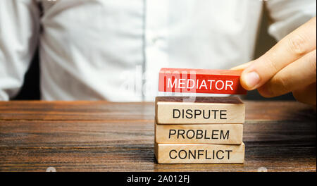 Ein Mann hält Holzblöcke mit dem Wort Mittler, Streit, Problem, Konflikt. Beilegung von Streitigkeiten durch Vermittler. Streitschlichtung und Mediation. Th Stockfoto