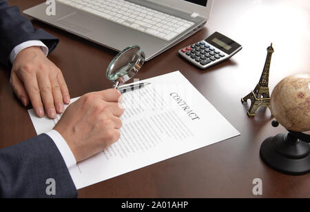 Hand eines Unternehmers an einen Vertrag Dokument mit der Lupe suchen. Stockfoto