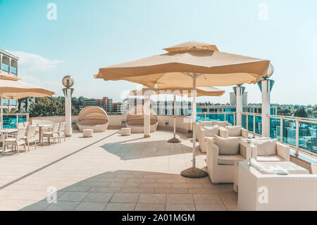 Großen weißen Sonnenschirm und Gartenmöbel Rattan Sofas und Stühle mit kissen und einen Tisch mit Glasplatte. Platz auf der Terrasse des Resort zum Entspannen Stockfoto