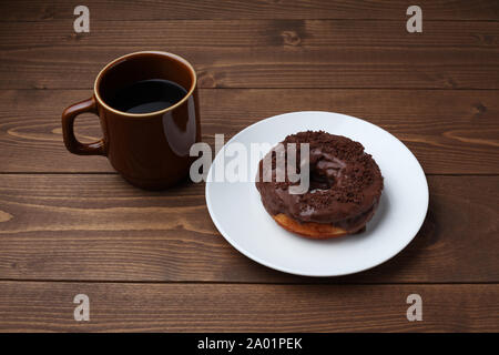 Schokolade matt Donut auf Platte mit heißem Kaffee closeup auf Holztisch, isoliert Stockfoto
