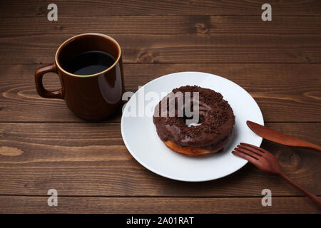 Schokolade matt Donut auf Platte mit heißem Kaffee closeup auf Holztisch, isoliert Stockfoto