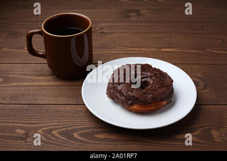 Schokolade matt Donut auf Platte mit heißem Kaffee closeup auf Holztisch, isoliert Stockfoto