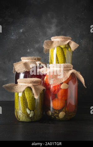 Obst- und Gemüsekonserven, Pflaume, Gurke, Tomate, die in Gläsern auf dunklen Holz- Board. Verschiedene Arten von Fermentiert. Vertikale Ausrichtung. Stockfoto