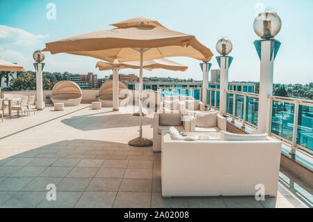 Großen weißen Sonnenschirm und Gartenmöbel Rattan Sofas und Stühle mit kissen und einen Tisch mit Glasplatte. Platz auf der Terrasse des Resort zum Entspannen Stockfoto
