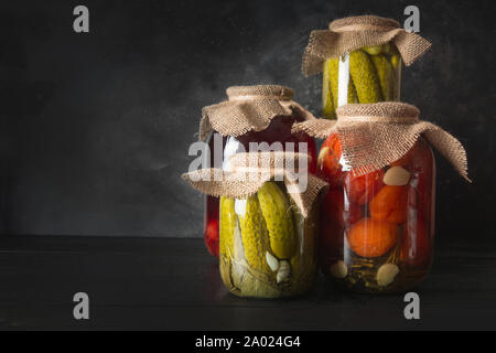 Konserven fermentierten Früchte und Gemüse, Pflaume, Gurke, Tomate, die in Gläsern auf dunklen Holz- Board. Verschiedene Arten von Fermentiert. Horizontale Ausrichtung. Stockfoto
