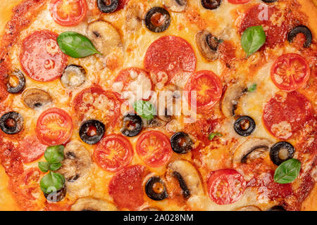 Pepperonipizza Textur mit pulsierenden Salamischeiben, schwarze Oliven, Champignons, frische Basilikumblätter und viel Käse Stockfoto